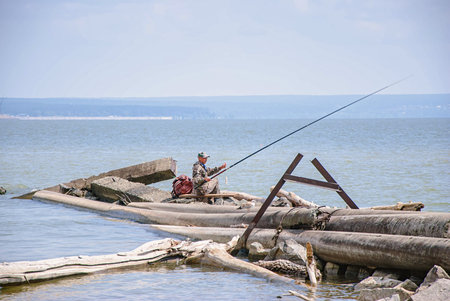 Fisherman sitting on a log and fishing in the sea.の写真素材