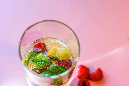 Refreshing drink with raspberries and mint in a glass on a pink backgroundの写真素材