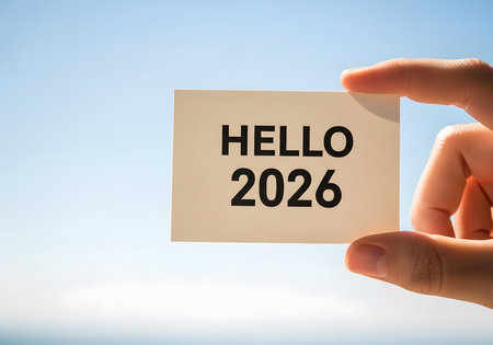 Hand holding a card with Hello 2026 message over blue sky backgroundの素材