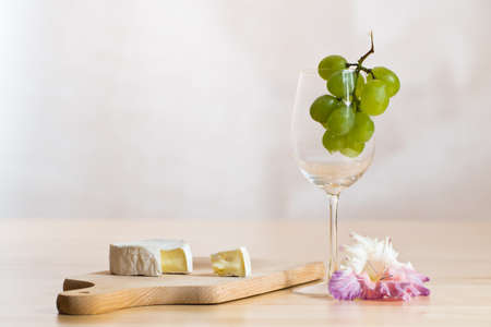 Bright still life photo of wine glass, cheese and blossomの写真素材