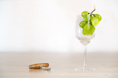Bright still life photo of wineglass with grape and corkscrew on white background