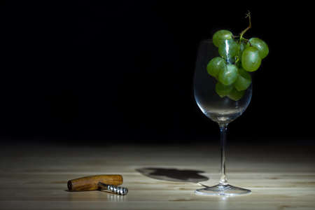 Dark still life photo of wineglass with grape and corkscrew on black backgroundの写真素材