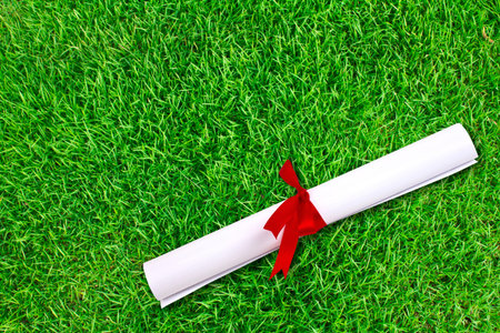 Diploma wrapped with a red ribbon on fresh spring green grass
