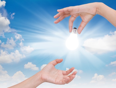 Women hand with lamp bulb against the blue sky.の写真素材