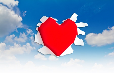Heart shape hole through paper over blue skyの写真素材