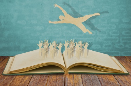 Paper cut of man jump over jubilant crowd on bookの写真素材