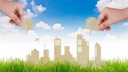 Woman hand put Paper cut of tree over  city and grass with blue skyの写真素材