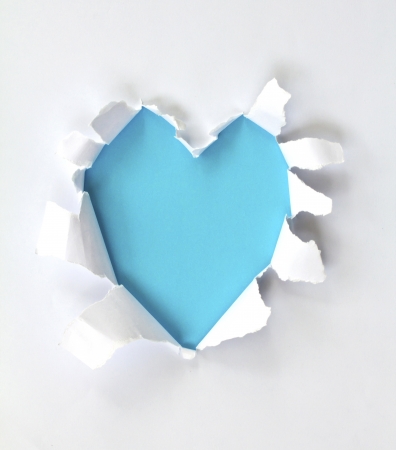 Sheet of paper with a Heart shape hole against bright blue background isolated on whiteの写真素材