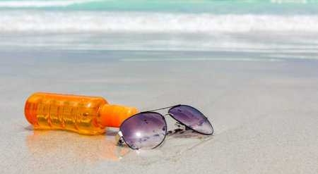 Sunscreen lotion and dark glasses on the beach for summer time