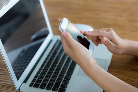 Closeup of business woman hand touch phone over laptop keyboard