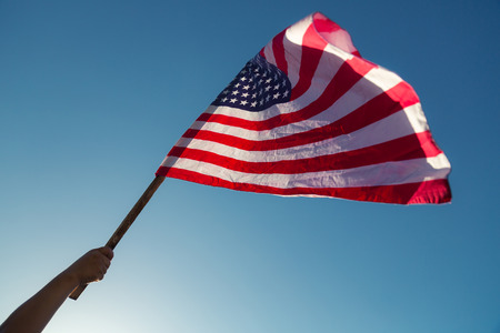 American flag with stars and stripes hold with hands against blue skyの写真素材