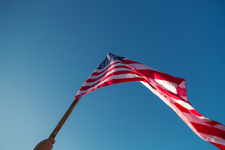 American flag with stars and stripes hold with hands against blue skyの写真素材