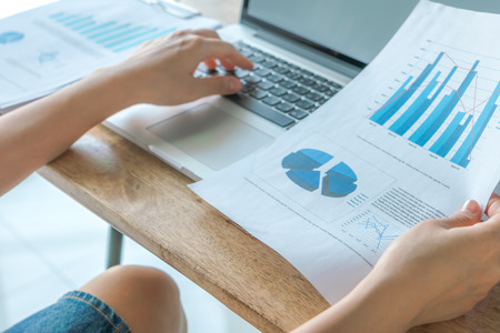 Business woman hand typing on laptop keyboard with Financial charts on the tableの写真素材