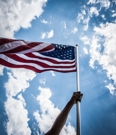 American flag with stars and stripes hold with hands against blue sky ( Filtered image processed vintage effect. )の写真素材