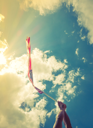 American flag with stars and stripes hold with hands against blue sky ( Filtered image processed vintage effect. )の写真素材