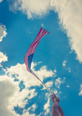 American flag with stars and stripes hold with hands against blue sky ( Filtered image processed vintage effect. )の写真素材