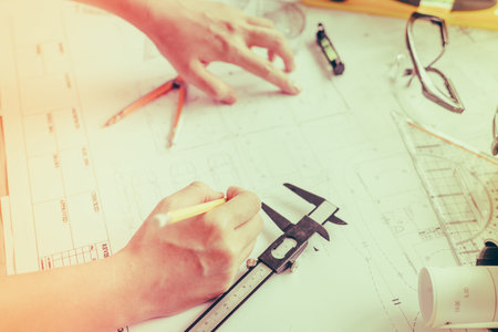 Hand over Construction plans with yellow helmet and drawing tools on blueprints ( Filtered image...