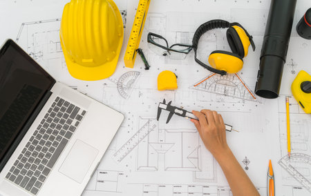 Hand over Construction plans with yellow helmet and drawing tools on blueprints