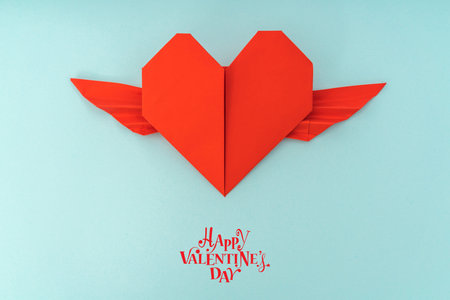 Red paper origami heart with wings on blue backgroundの写真素材