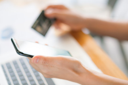Hands holding a credit card using laptop computer and mobile phone for online shopping .