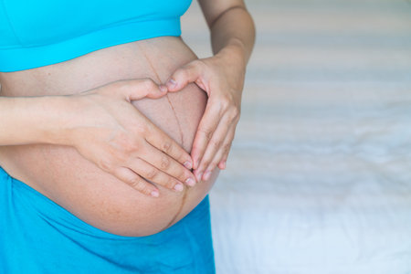 Woman holding her hands in a heart shape on her pregnant belly.