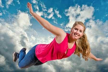 Young girl is flying in clouds in front of blue skyの写真素材