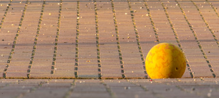 Yellow Kids Ball Lies on a Paved Place in front of Blurred Background