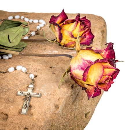 Christian cross on rosary and a dry yellow red roses lie on a sandstoneの写真素材