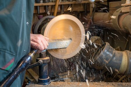 Making a wooden bowl on a lathe in an old small workshop with flying wooden shavingsの写真素材