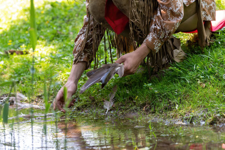 Man in Indian clothing picks up a bird's feather in a meadow on the banks of a streamの写真素材