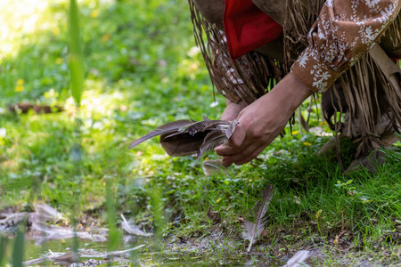 Man in Indian clothing picks up a bird's feather in a meadow on the banks of a streamの写真素材