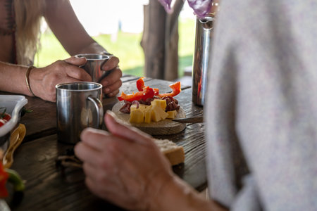 Wooden board with cheese, sausage and paprika stands on a rustic table between peopleの写真素材
