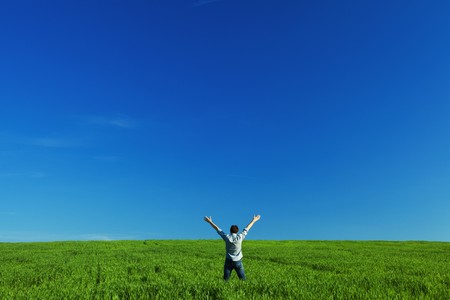 young man outstretched arms in green field against the blue skyの写真素材