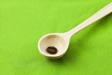 coffee beans in a wooden spoon on a green backgroundの写真素材
