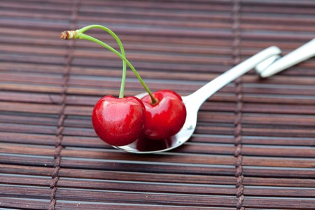cherry in spoon on a bamboo matの写真素材
