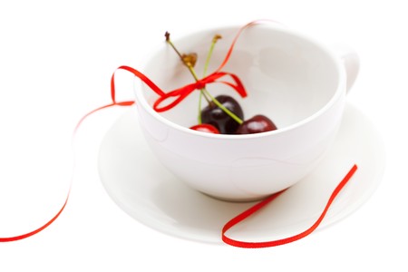 cup saucer  and cherries with ribbon isolated on whiteの写真素材