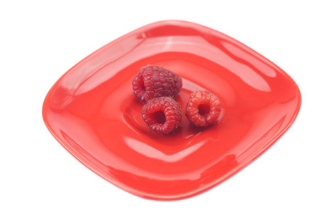 Raspberries in a red saucer isolated on white