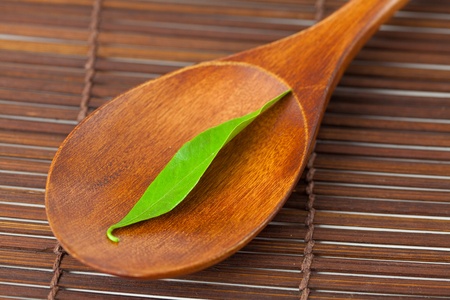 green leaf on the wooden spoon on a bamboo matの写真素材