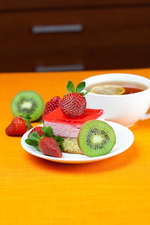 lemon tea, kiwi,cake and strawberries lying on the orange fabricの写真素材