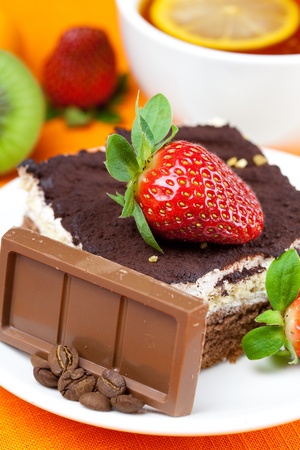 lemon tea,chocolate, kiwi,cake and strawberries lying on the orange fabricの写真素材