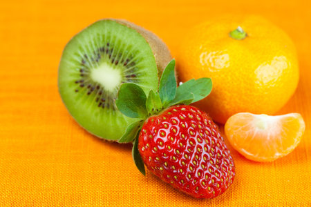 kiwi,mandarin and strawberries lying on the orange fabricの写真素材