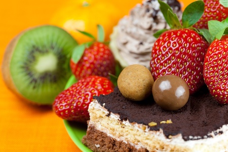 cake, chocolate candy, tangerine, kiwi and strawberries on the orange fabricの写真素材