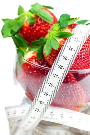 big juicy red ripe strawberries in a glass bowl and measure tape isolated on whiteの写真素材