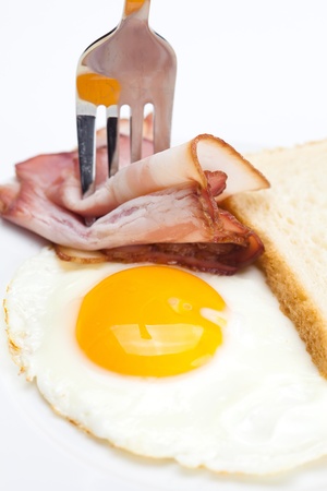 bacon with  fried  eggs on a plate, fork and bread isolated on whiteの写真素材