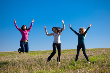 three young beautiful woman jumping into the field against the sky