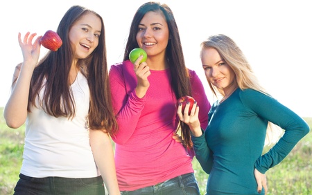 portret of three young beautiful woman with apple on the  sky background の写真素材