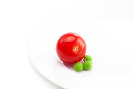 tomato and peas on a plate isolated on whiteの写真素材