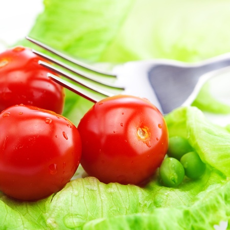 tomato,peas and lettuce with a fork on a plate isolated on whiteの写真素材