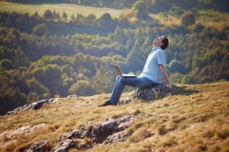young man using laptop sitting on the grass on the hillsideの写真素材