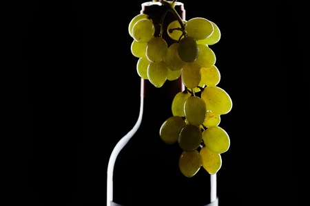 bottle of wine and a bunch of grapes on a black backgroundの写真素材